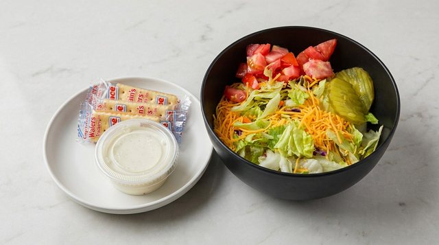 Side salad with lettuce, tomato, shredded cheddar and a pickle, served with dressing and crackers, at Betty's Bar-B-Q in Anniston, AL